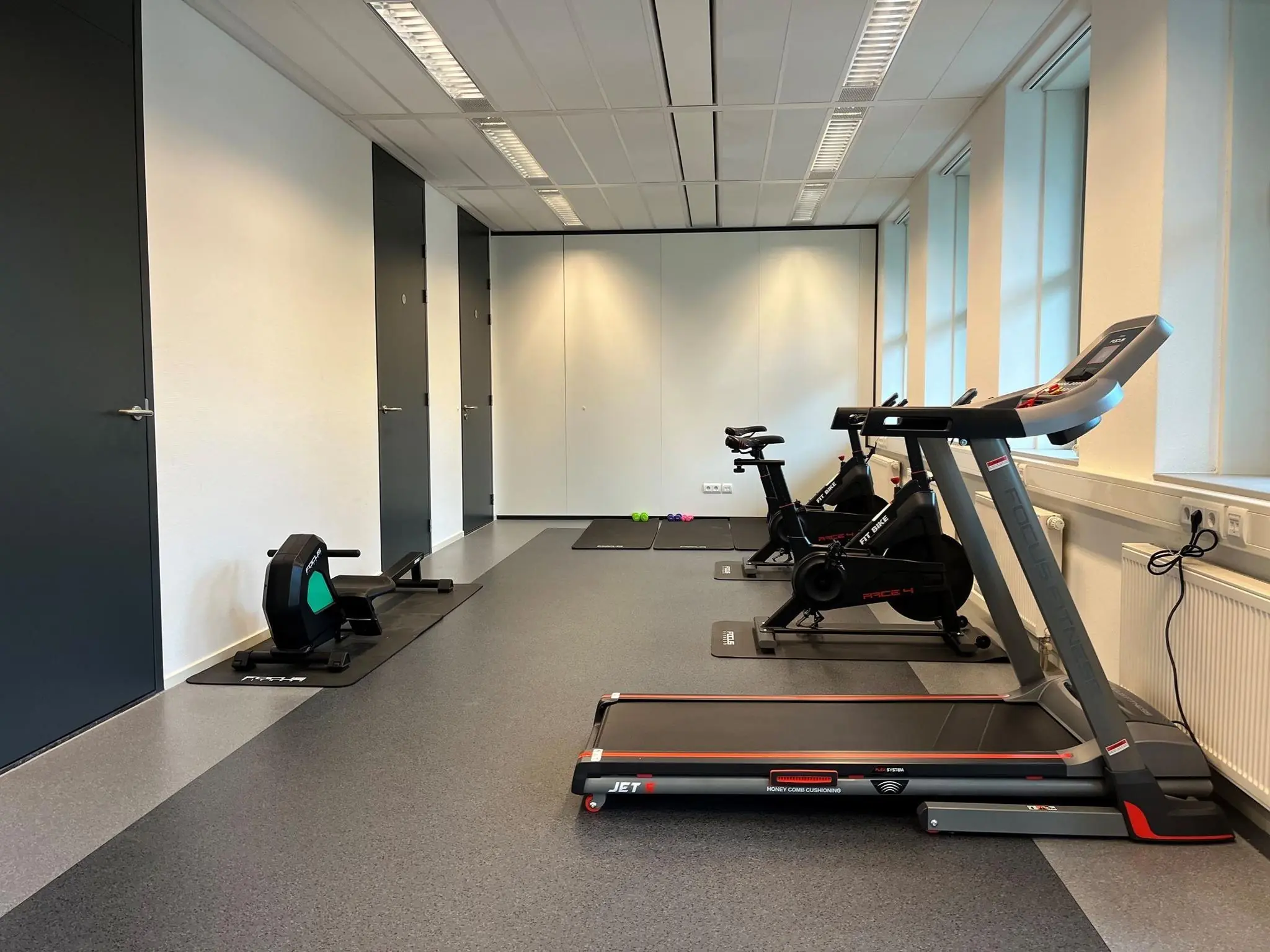 Kleine fitnessruimte bij De Wel met een loopband, hometrainers en roeimachine.